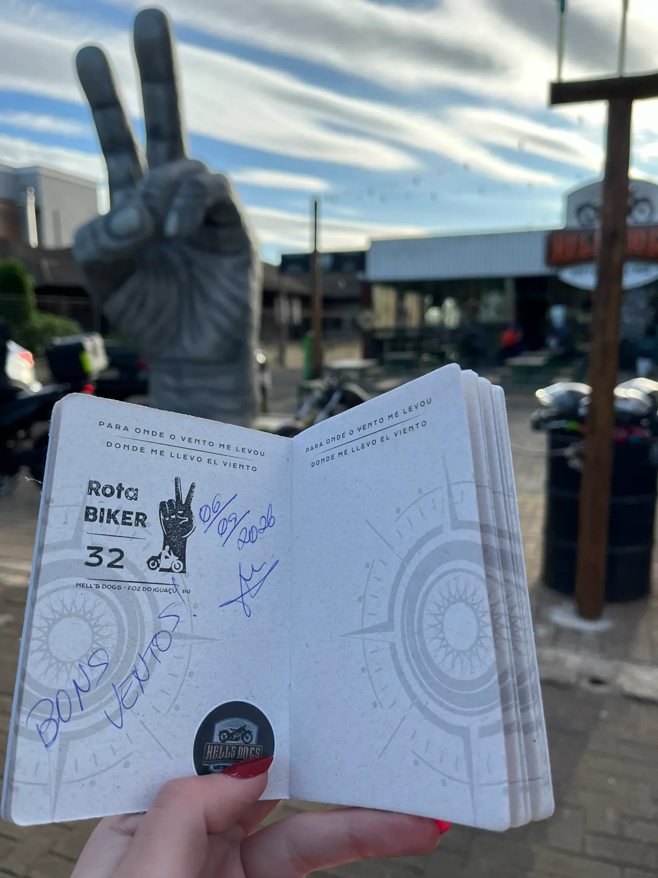 Passaporte da Rota Biker com o registro do monumento 32 diante do monumento em Foz do Iguaçu